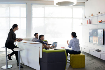 Group using laptops and screens in a modern office lounge, discussing technology solutions