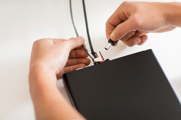 Hands connecting power cable and security lock to black laptop, preloved tech device